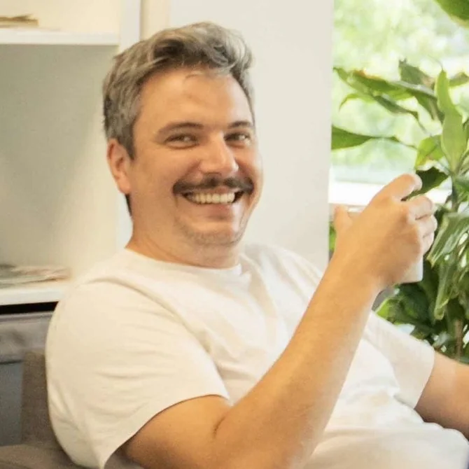 Anton Hannig sitzt lachend im Sessel, eine Kaffeetasse in der Hand.