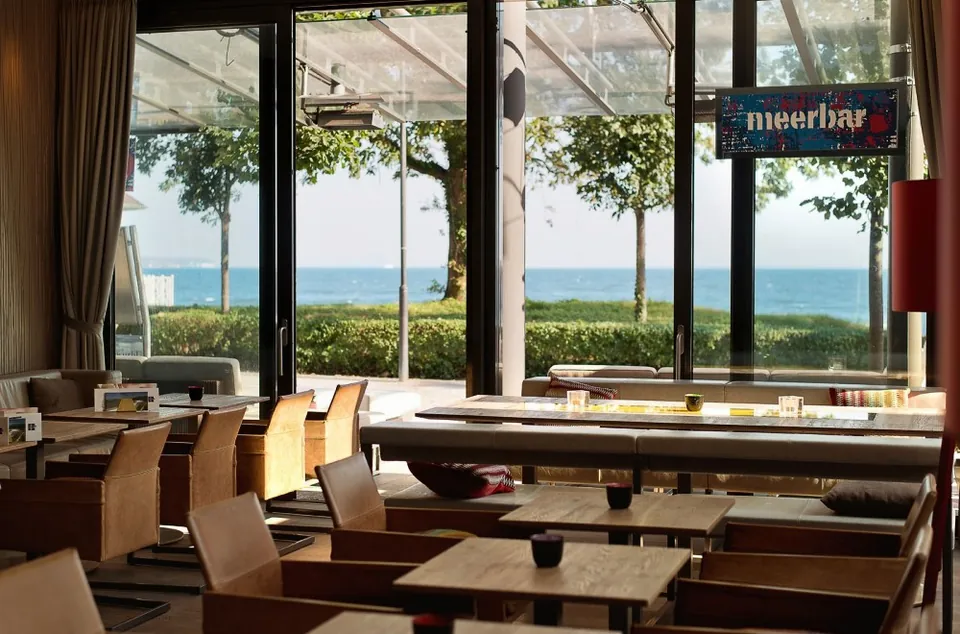 Blick aus der meerbar durch deckenhohe Fenster auf Strand und Ostsee