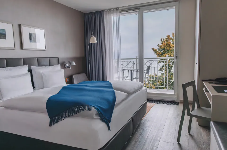 Doppelzimmer mit hellem Holzboden, großem Bett und Balkontür